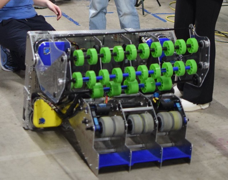 A FIRST Robotics competition robot on the floor, showing rows of green rollers and a metal collector