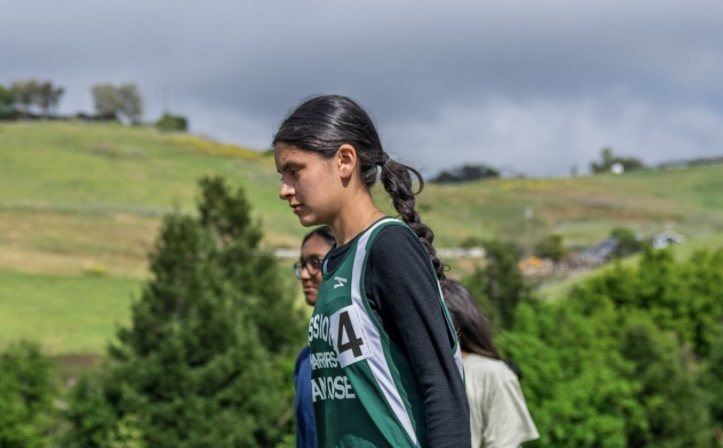 Afrah Nazar running in a Mission San Jose jersey on a hillside course